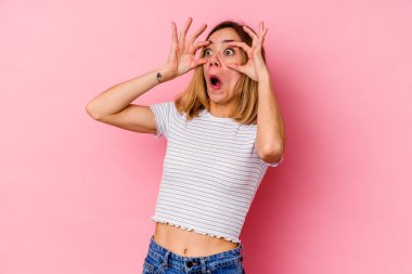 Pembe arka planda izole edilmiş genç beyaz kadın bir başarı fırsatı bulmak için gözlerini açık tutuyor..