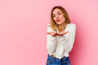 Beyaz bir kadın pembe arka planda izole edilmiş dudaklar kıvrılmış ve hava öpücüğü göndermek için avuç içleri tutulmuş..