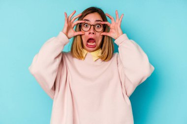 Mavi arka planda izole edilmiş genç beyaz kadın başarı fırsatı bulmak için gözlerini açık tutuyor..