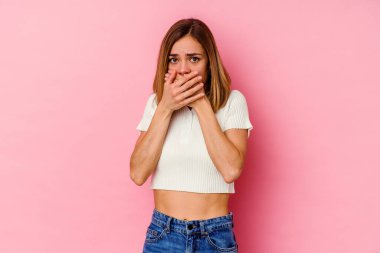 Pembe arka planda izole edilmiş genç, beyaz bir kadın elleri endişeli bir şekilde ağzı örtüyor..