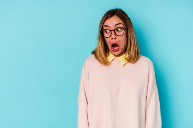 Mavi arka planda izole genç beyaz kadın gördüğü bir şey yüzünden şoka uğruyor..