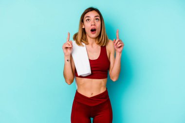 Mavi arka planda izole edilmiş genç beyaz kadın ağzı açık bir şekilde üst tarafı işaret ediyor..