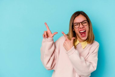 Mavi arka planda izole edilmiş genç beyaz bir kadın işaret parmağıyla fotokopi alanını işaret ederek heyecan ve arzusunu ifade ediyor..