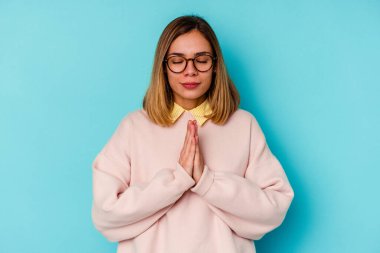 Mavi arka planda izole edilmiş genç beyaz bir kadın el ele tutuşup dua ediyor, kendinden emin hissediyor..