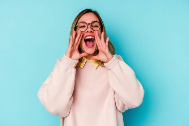 Genç beyaz kadın, mavi arka planda izole edilmiş, heyecanlı bir şekilde bağırıyor..
