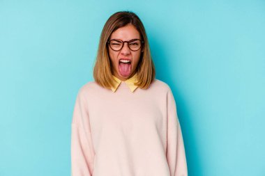 Genç beyaz bir kadın öğrenci mavi arka planda izole edilmiş komik ve dost canlısı bir dil kullanıyor..