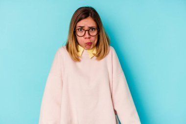 Mavi arka planda izole genç beyaz kadın yanakları patlatıyor, yorgun bir ifadesi var. Yüz ifadesi kavramı.