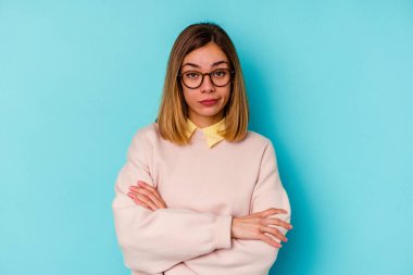 Genç beyaz kadın, mavi arka planda izole edilmiş. Mutsuz, alaycı bir ifadeyle kameraya bakıyor..