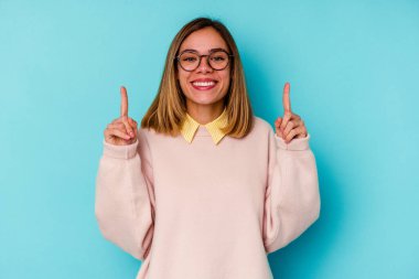 Mavi arka planda izole genç beyaz kadın iki parmağı da boş bir alan gösteriyor..