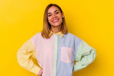 Sarı arka planda izole edilmiş beyaz tenli genç bir kadın ellerini kalçasında tutuyor..