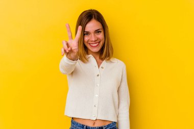 Sarı arka planda izole edilmiş genç beyaz kadın zafer işareti gösteriyor ve gülümsüyor..
