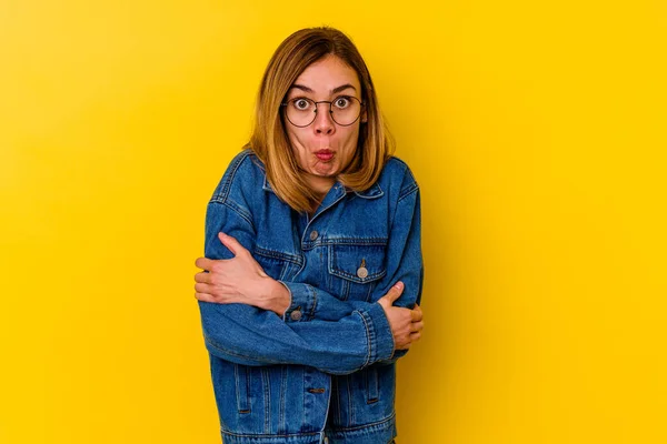 Young caucasian skinny woman isolated on yellow background shrugs shoulders and open eyes confused.