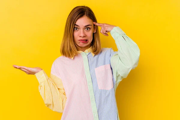 Young caucasian skinny woman isolated on yellow background holding and showing a product on hand.