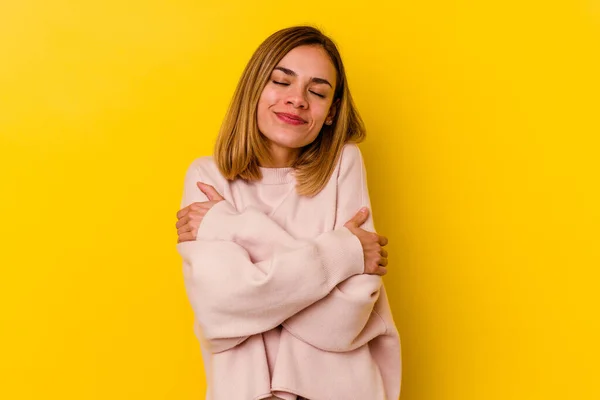 Young caucasian skinny woman isolated on yellow background hugs, smiling carefree and happy.