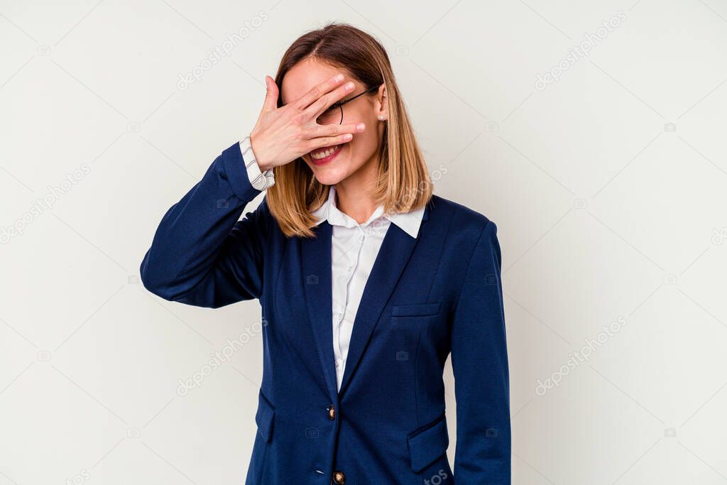 Young business caucasian woman isolated on white background blink at the camera through fingers, embarrassed covering face.