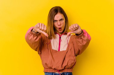 Sarı arka planda izole edilmiş genç beyaz kadın baş parmağını aşağı gösteriyor ve hoşlanmadığını ifade ediyor..