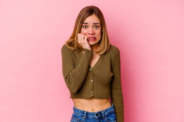 Pembe arka planda izole edilmiş, tırnak yiyen, gergin ve endişeli bir beyaz kadın..