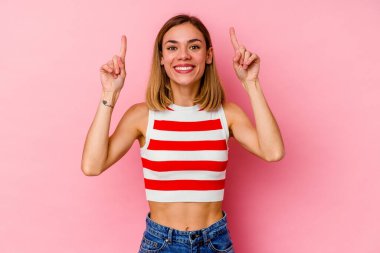Pembe arka planda izole edilmiş genç beyaz kadın iki parmağı da boş bir alan gösteriyor..