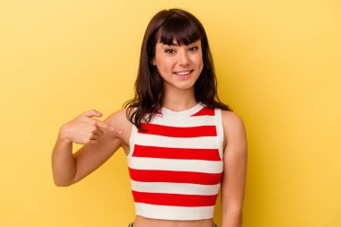 Sarı arka planda izole edilmiş genç beyaz bir kadın gömleğin fotokopi odasını elle işaret ediyor, gururlu ve kendinden emin.