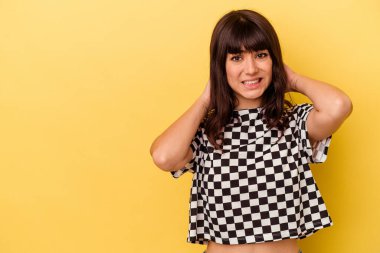 Kafkasyalı genç bir kadın sarı arka planda izole edilmiş kafasının arkasına dokunuyor, düşünüyor ve bir seçim yapıyor..