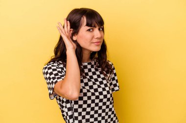 Sarı arka planda izole edilmiş genç beyaz kadın bir dedikoduyu dinlemeye çalışıyor..