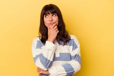 Kafkasyalı genç bir kadın sarı arka planda izole edilmiş düşünüyor ve yukarı bakıyor, yansıtıyor, düşünüyor, hayal kuruyor..