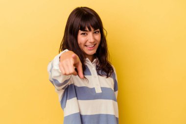 Sarı arka planda izole edilmiş genç beyaz kadın parmaklarıyla ön tarafı işaret ediyor..