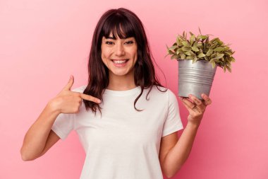 Pembe arka plandaki bir bitkiyi elinde tutan beyaz bir kadın gömlek fotokopi alanını işaret ediyor, gururlu ve kendinden emin.