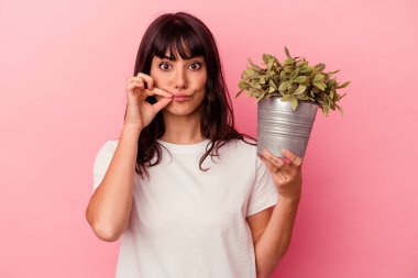 Pembe arka planda bir bitkiyi tutan beyaz bir kadın parmakları dudaklarında bir sır saklıyor..