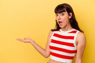 Sarı arka planda izole edilmiş genç beyaz kadın avuç içinin fotokopi alanını elinde tutmaktan etkilenmiş..