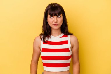 Sarı arka planda izole edilmiş genç beyaz kadın kafası karışmış, kuşkulu ve kendinden emin değil..