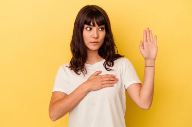 Sarı arka planda izole edilmiş genç beyaz kadın yemin ediyor, elini göğsüne koyuyor..