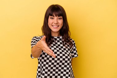 Sarı arka planda izole edilmiş genç beyaz kadın selamlaşma jesti olarak kameraya elini uzatıyor..