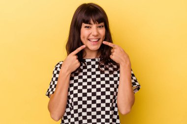 Sarı arka planda izole edilmiş genç beyaz kadın gülümsüyor, parmaklarını ağzına doğrultuyor..