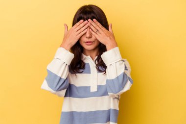 Sarı arka planda izole edilmiş genç beyaz kadın elleriyle gözlerini kapatmaktan korkuyor..