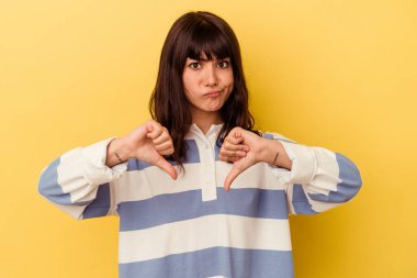 Sarı arka planda izole edilmiş genç beyaz kadın baş parmağını aşağı gösteriyor, hayal kırıklığı konsepti..