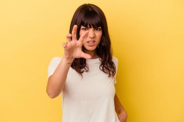 Sarı arka planda izole edilmiş genç beyaz kadın pençelerini kedi taklidi yaparken gösteriyor, agresif bir hareket..