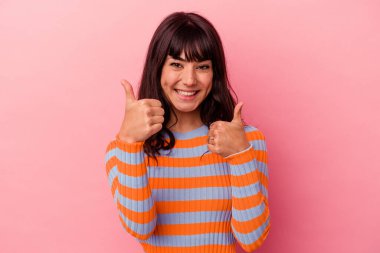 Pembe arka planda izole edilmiş genç beyaz kadın iki parmağını da kaldırıyor, gülümsüyor ve kendinden emin..