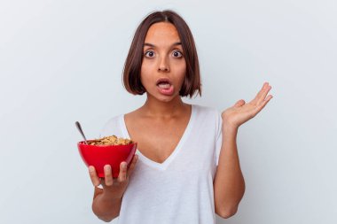 Beyaz arka planda izole edilmiş mısır gevreği yiyen genç bir ırk kadını şaşırdı ve şok oldu..