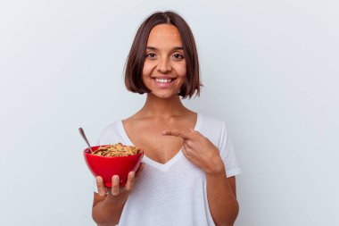 Beyaz arka planda izole edilmiş mısır gevreği yiyen genç bir ırk kadını gülümsüyor ve boş alanda bir şeyler gösteriyor..