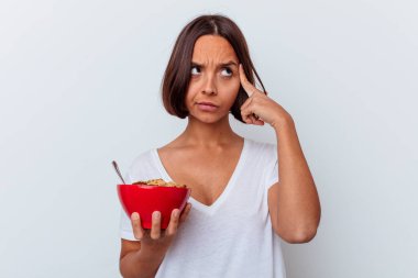 Beyaz arka planda izole edilmiş mısır gevreği yiyen genç bir ırk kadını şakağı işaret ediyor, düşünüyor ve bir göreve odaklanıyor..