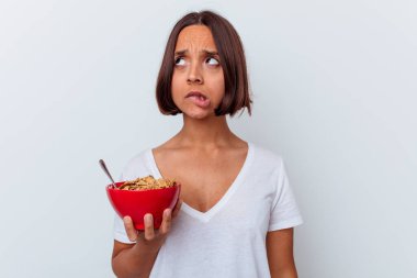 Beyaz arka planda izole edilmiş mısır gevreği yiyen genç bir ırk kadının kafası karışmış, kuşkulu ve kendinden emin değil..