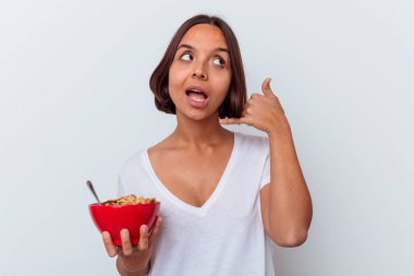 Beyaz arka planda izole edilmiş mısır gevreği yiyen genç bir ırk kadını parmaklarıyla bir cep telefonu çağrısı hareketi gösteriyor..