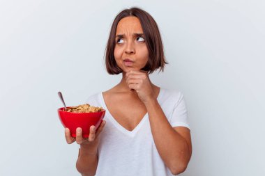 Beyaz arka planda izole edilmiş mısır gevreği yiyen genç bir ırk kadını şüpheli ve şüpheci bir ifadeyle yana bakıyor..