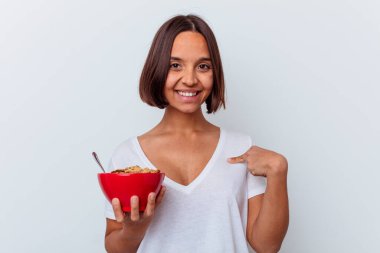 Beyaz arka planda izole edilmiş mısır gevreği yiyen genç bir ırk kadını gömlek fotokopi alanını işaret ediyor, gururlu ve kendinden emin.