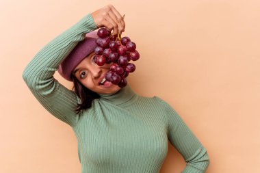 Bej arka planda üzüm tutan genç melez kadın.