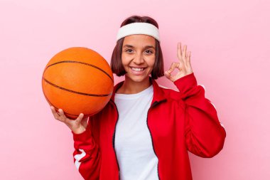 Basketbol oynayan genç melez kadın pembe arka planda izole edilmiş neşeli ve kendinden emin..