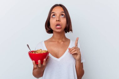 Beyaz arka planda izole edilmiş mısır gevreği yiyen genç bir ırk kadını ağzı açık bir şekilde üst tarafı işaret ediyor..