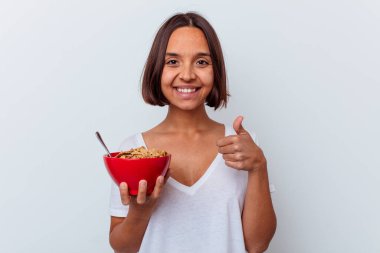 Beyaz arka planda izole edilmiş mısır gevreği yiyen genç bir ırk kadını gülümsüyor ve başparmağını kaldırıyor.