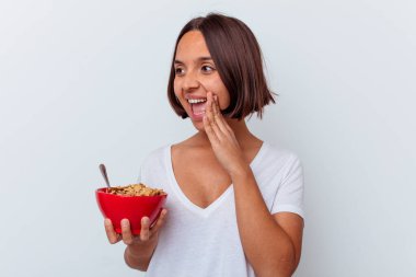 Beyaz arka planda izole edilmiş mısır gevreği yiyen genç bir ırk kadını bağırıyor ve avuç içini açık tutuyor..